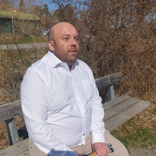 En ung man i vit skjorta sitter på en bänk utomhus